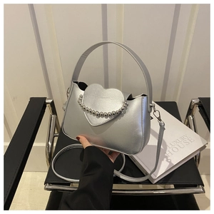 Detail of silver metallic handbag featuring heart-shaped flap and polished bead chain