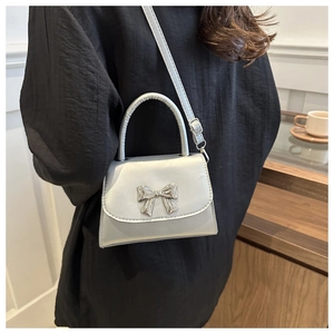 Silver metallic crossbody bag with a bow buckle shown on a model in a minimalist setting