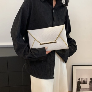 Pochette enveloppe blanche tressée avec bordure dorée portée par un mannequin chic