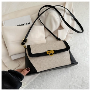 Detailed close-up of beige canvas crossbody bag with black leather trim and gold U-lock