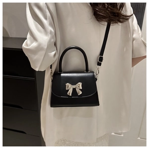 Detail of black crossbody bag with silver bow hardware worn by a model in a casual setting
