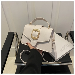 Detail view of white lychee-grain leather handbag with large gold buckle on modern chair