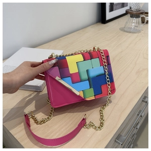 Detail of color-block crossbody bag with magenta panels and golden chain strap on a desk