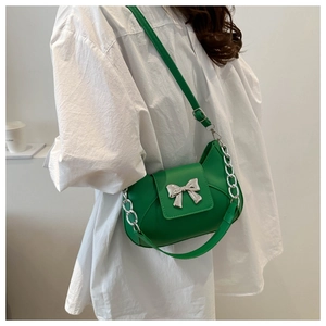 Dettaglio della borsa a tracolla verde con fiocco argento e catena in metallo su modella