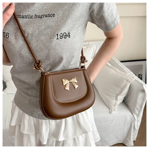 Detail of brown saddle bag with golden bow clasp and stylish knotted shoulder strap
