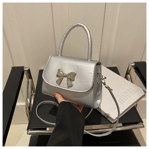Detail of silver shoulder bag with metallic bow decoration on a modern chair