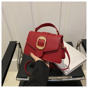 Detail of red textured leather handbag with gold buckle and top handle held by hand