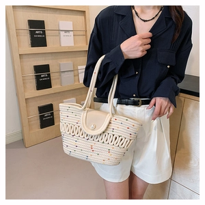 Detail of woven straw tote bag with colorful pom-poms and large pearl closure