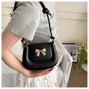 Detail of a black leather shoulder bag with a gold bow accent worn by a model