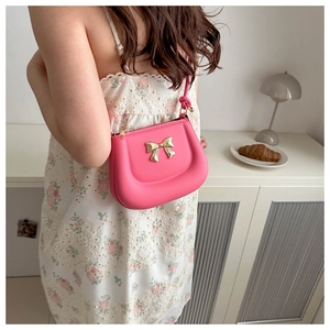 Chic pink crossbody bag with gold bow detail and knotted shoulder strap in lifestyle setting