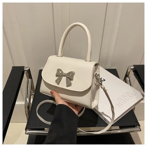 Close-up of white crossbody bag with a polished silver metal bow and magnetic flap
