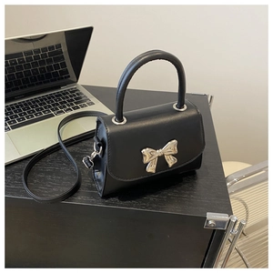 Detail of black leather crossbody bag featuring a stylish silver metal bow decoration