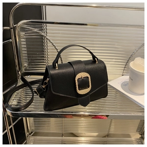 Detail of black lychee grain leather handbag with prominent gold buckle and shoulder strap