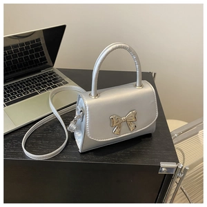 Detail of silver metallic square bag featuring a gold bow accent and leather handle
