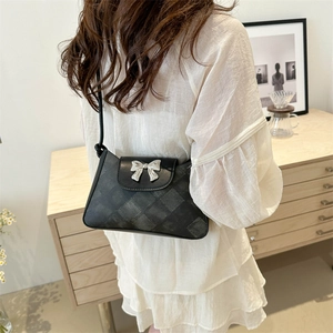 Chic black crossbody bag with checkered texture and silver bow detail worn by model