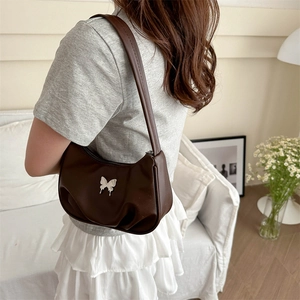 Brown half-moon underarm bag with silver butterfly accent on a soft white sofa