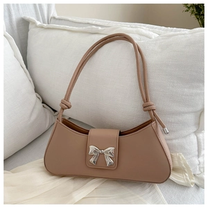 Detail of light brown shoulder bag with silver bow clasp on a soft white pillow