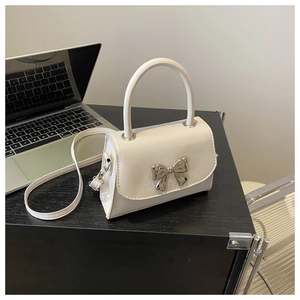 Close-up of white crossbody bag with silver metal bow detail on a desk setting