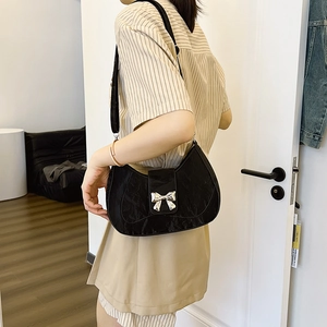 Fashionable black pleated crescent shoulder bag with silver bow hardware worn by a model