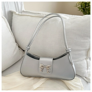 Silver shoulder bag with metallic bow detail and knotted handles on white soft pillows