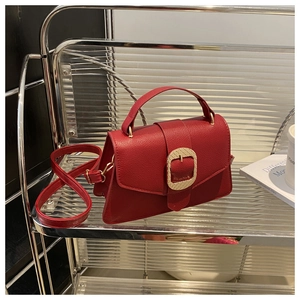 Detail of red lychee grain leather handbag with gold woven buckle on glass shelf