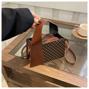 Détail du sac à main en cuir marron avec monogramme doré posé sur une table en verre