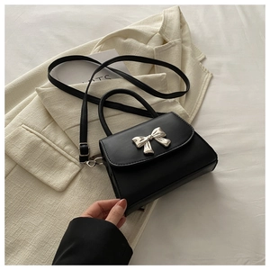 Detail of a black square bag featuring a silver bow metal buckle and matte leather texture