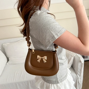 Brown semi-circular shoulder bag with a gold bow detail and knotted handle strap