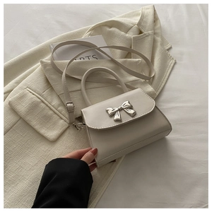 Detail of cream crossbody bag with silver bow accent and adjustable shoulder strap