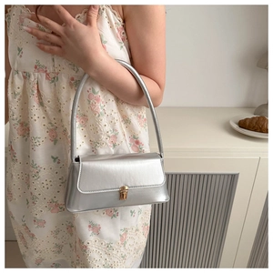 Detail of silver baguette underarm bag featuring a gold clasp on a floral dress model