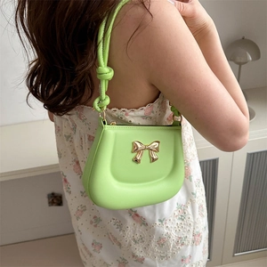 Fluorescent green shoulder bag with gold bow clasp worn by a model in a casual setting