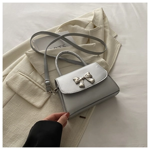 Detail of silver crossbody bag featuring a metallic bow buckle and adjustable strap