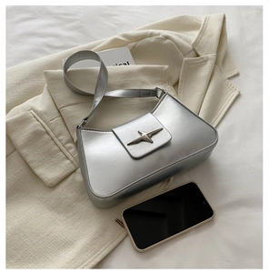 Detail view of silver baguette bag with a metal star ornament on a soft blazer backdrop