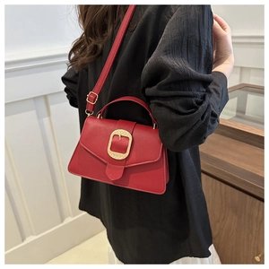 Detailed close-up of a red leather crossbody bag with a large textured golden buckle