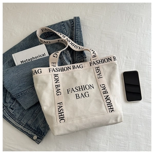 Gros plan sur l'imprimé noir 'FASHION BAG' d'un grand sac cabas en toile de couleur crème