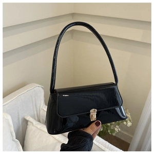 Detail of glossy black patent leather baguette bag with a sleek metallic buckle closure