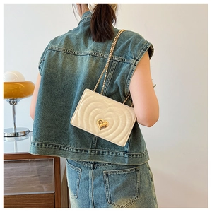 Detailed view of cream heart-quilted crossbody bag with gold chain strap and heart twist lock