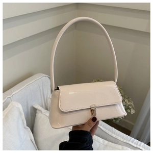 Detail of glossy patent leather cream shoulder bag with minimalist golden metal buckle