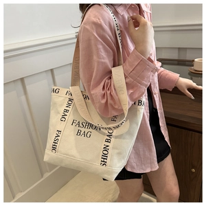 Gros plan d'un sac cabas en toile beige avec imprimé lettrage noir et larges anses en tissu
