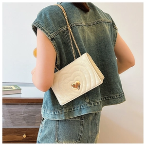 Close-up of white quilted chain bag with gold heart-shaped lock worn by a model