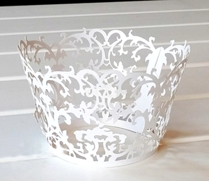 Macro detail of laser-cut white cupcake wrapper featuring intricate lace and vine patterns