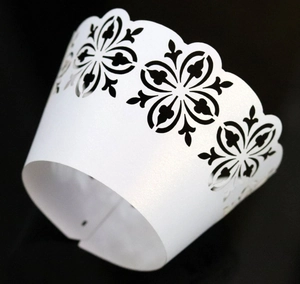 Detailed view of laser-cut white cupcake wrapper with elegant black floral scroll patterns