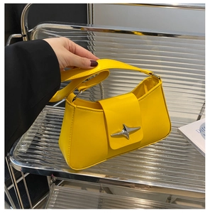 Detail of yellow leather shoulder bag with star-shaped silver buckle on metal shelf