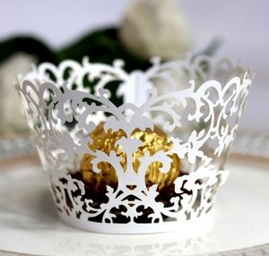 White laser-cut cupcake wrappers with intricate vine patterns for wedding celebration