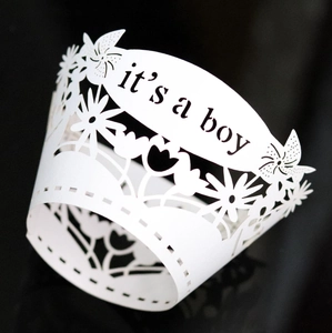 Detail of white laser-cut 'it's a boy' cupcake wrappers with intricate floral patterns