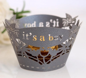 Macro detail of 'it's a boy' laser-cut paper cupcake wrapper with floral hollow patterns