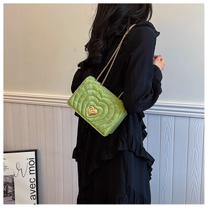 Close-up of green heart-quilted chain bag with golden heart lock on a black dress