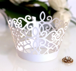Close-up of laser-cut white lace cupcake wrappers with elegant scroll patterns for weddings