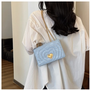 Close-up of heart-quilted light blue chain bag with golden heart lock worn by model
