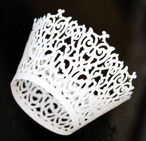 Macro detail of laser-cut white cupcake wrapper with floral and crown hollow design